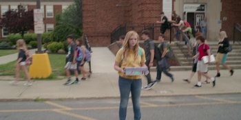 Movie still from “Eighth Grade” (2018), directed by Bo Burnham – A girl is holding a skateboard while standing on the sidewalk; Wide shot, Over the shoulder angle