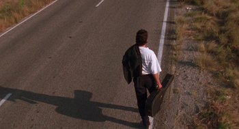 Movie still from “El Mariachi” (1992), directed by Robert Rodriguez – A man walking down a street holding a guitar case; Wide shot, Low angle