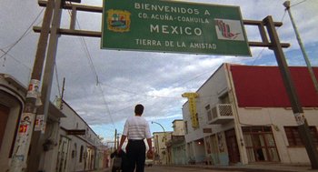 Movie still from “El Mariachi” (1992), directed by Robert Rodriguez – A man standing under a street sign in a foreign country; Extreme Wide shot, Low angle