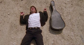 Movie still from “El Mariachi” (1992), directed by Robert Rodriguez – A man laying on the ground next to a guitar case; Medium shot, Overhead angle