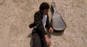 Movie still from “El Mariachi” (1992), directed by Robert Rodriguez – A man sitting on the ground next to a guitar case; Medium shot, Overhead angle