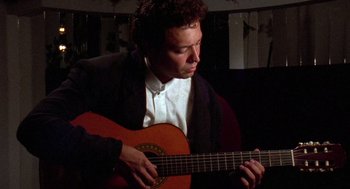 Movie still from “El Mariachi” (1992), directed by Robert Rodriguez – A man in a white shirt and jacket playing a guitar; Close Up shot, Low angle