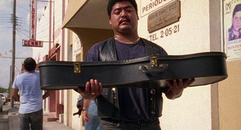 Movie still from “El Mariachi” (1992), directed by Robert Rodriguez – A man holding a guitar case on the side of the street; Medium shot, Low angle