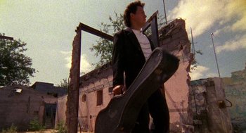 Movie still from “El Mariachi” (1992), directed by Robert Rodriguez – A man holding a guitar case walking down a street; Medium shot, Low angle
