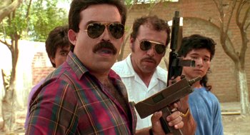Movie still from “El Mariachi” (1992), directed by Robert Rodriguez – A man in plaid shirt and sunglasses holding a gun; Medium shot, Low angle