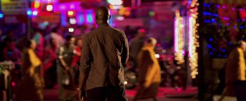 Movie still from “Elephant White” (2011), directed by Prachya Pinkaew – A man standing on the street in front of a crowd of onlookers at night; Medium shot, Over the shoulder angle