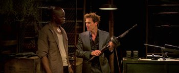 Movie still from “Elephant White” (2011), directed by Prachya Pinkaew – A man in a suit holding a blow dryer in his hand; Medium shot, Over the shoulder angle