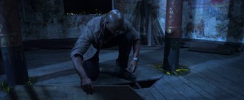 Movie still from “Elephant White” (2011), directed by Prachya Pinkaew – A man kneeling down on the ground looking down; Wide shot, Overhead angle