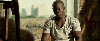 Movie still from “Elephant White” (2011), directed by Prachya Pinkaew – A man sitting on top of a stone wall; Close Up shot, Low angle