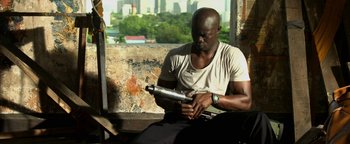 Movie still from “Elephant White” (2011), directed by Prachya Pinkaew – A man sitting on a chair holding a gun; Medium shot, High angle