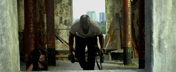 Movie still from “Elephant White” (2011), directed by Prachya Pinkaew – A man is bending over with a skateboard in his hand; Wide shot, Low angle