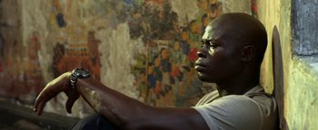 Movie still from “Elephant White” (2011), directed by Prachya Pinkaew – A man sitting in front of a wall painting; Close Up shot, Low angle