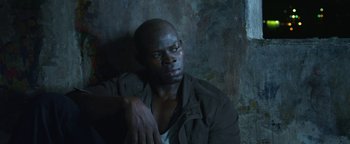 Movie still from “Elephant White” (2011), directed by Prachya Pinkaew – A man sitting against a wall with his hand on his chest; Close Up shot, High angle