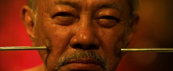 Movie still from “Elephant White” (2011), directed by Prachya Pinkaew – An older man with a beard and mustache; Extreme Close Up shot, High angle