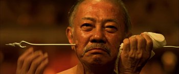 Movie still from “Elephant White” (2011), directed by Prachya Pinkaew – An old man with a mustache and a beard is talking on the phone; Extreme Close Up shot, Low angle
