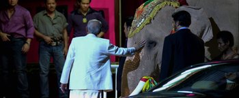 Movie still from “Elephant White” (2011), directed by Prachya Pinkaew – An older man touching an elephant's trunk with his hand; Wide shot, Over the shoulder angle