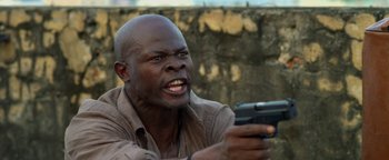 Movie still from “Elephant White” (2011), directed by Prachya Pinkaew – A man holding a gun while wearing a brown shirt; Close Up shot, Low angle