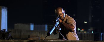 Movie still from “Elephant White” (2011), directed by Prachya Pinkaew – A man is holding a rifle and aiming it at night; Medium shot, Low angle