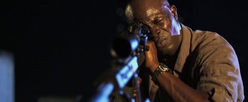 Movie still from “Elephant White” (2011), directed by Prachya Pinkaew – A man is holding a rifle and looking through the scope; Close Up shot, High angle