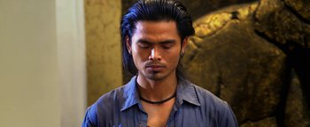 Movie still from “Elephant White” (2011), directed by Prachya Pinkaew – A man with long black hair wearing a blue shirt; Close Up shot, Low angle