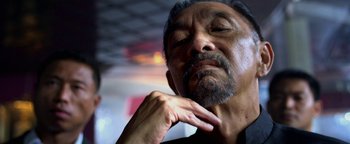 Movie still from “Elephant White” (2011), directed by Prachya Pinkaew – An older man with a beard is touching his chin; Close Up shot, Low angle