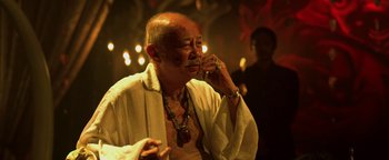 Movie still from “Elephant White” (2011), directed by Prachya Pinkaew – An older man talking on a cell phone in front of candles; Close Up shot, Over the shoulder angle