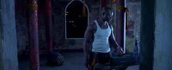 Movie still from “Elephant White” (2011), directed by Prachya Pinkaew – A man in a white tank top is standing in front of a window; Medium shot, Low angle