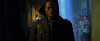 Movie still from “Elephant White” (2011), directed by Prachya Pinkaew – A man wearing a hooded jacket standing in the rain; Close Up shot, Low angle