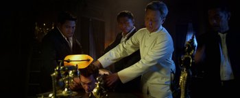 Movie still from “Elephant White” (2011), directed by Prachya Pinkaew – A group of people standing around a table; Medium shot, Low angle
