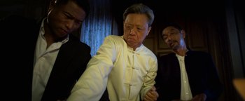 Movie still from “Elephant White” (2011), directed by Prachya Pinkaew – An older man in a white shirt is being held by two other men; Medium shot, Low angle