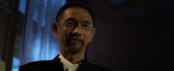 Movie still from “Elephant White” (2011), directed by Prachya Pinkaew – An older man wearing a black suit and white shirt; Close Up shot, Low angle