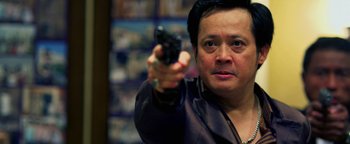 Movie still from “Elephant White” (2011), directed by Prachya Pinkaew – A man holding a gun in his right hand while wearing a leather jacket; Close Up shot, Low angle