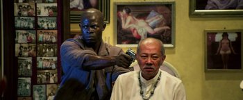 Movie still from “Elephant White” (2011), directed by Prachya Pinkaew – A man getting his hair cut by another man; Medium shot, Over the shoulder angle