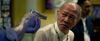Movie still from “Elephant White” (2011), directed by Prachya Pinkaew – An older man is holding a gun in his hand; Close Up shot, Over the shoulder angle