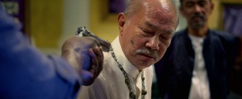 Movie still from “Elephant White” (2011), directed by Prachya Pinkaew – An older man is holding a pair of shears; Close Up shot, Over the shoulder angle