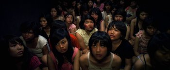 Movie still from “Elephant White” (2011), directed by Prachya Pinkaew – A large group of people sitting in a room; Medium shot, High angle