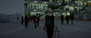 Movie still from “Ema” (2019), directed by Pablo Larraín – A woman with a backpack walking in a building with stairs; Wide shot, Low angle