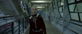 Movie still from “Ema” (2019), directed by Pablo Larraín – A woman in a black and white striped shirt is walking down a hallway; Medium shot, Low angle