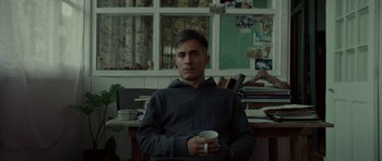 Movie still from “Ema” (2019), directed by Pablo Larraín – A man holding a coffee cup in a room; Medium shot, High angle