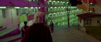 Movie still from “Ema” (2019), directed by Pablo Larraín – A woman standing in front of a building at night; Wide shot, Over the shoulder angle