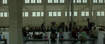 Movie still from “Ema” (2019), directed by Pablo Larraín – A group of people sitting in a large room; Extreme Wide shot, High angle