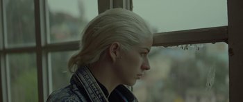 Movie still from “Ema” (2019), directed by Pablo Larraín – A woman sitting in front of a window with her head turned to the side; Close Up shot, Low angle