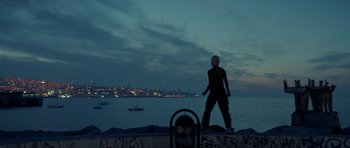 Movie still from “Ema” (2019), directed by Pablo Larraín – A person standing on a rock near the ocean; Extreme Wide shot, Low angle