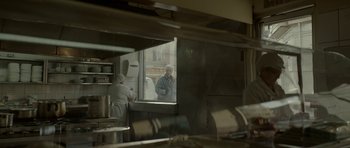 Movie still from “Ema” (2019), directed by Pablo Larraín – A man standing next to a window in a kitchen; Medium shot, Over the shoulder angle