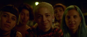 Movie still from “Ema” (2019), directed by Pablo Larraín – A woman with blonde hair is smiling for the camera; Close Up shot, Over the shoulder angle