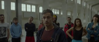 Movie still from “Ema” (2019), directed by Pablo Larraín – A group of people standing in a room; Medium shot, Low angle