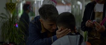 Movie still from “Ema” (2019), directed by Pablo Larraín – A man is touching the ear of a young boy; Close Up shot, Over the shoulder angle