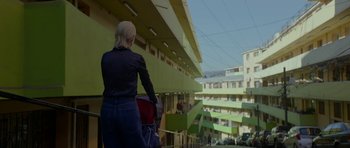 Movie still from “Ema” (2019), directed by Pablo Larraín – A woman standing on the side of a building with a bag; Wide shot, Low angle
