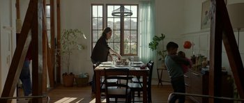 Movie still from “Ema” (2019), directed by Pablo Larraín – A person standing at a table with a plate of food; Wide shot, Low angle