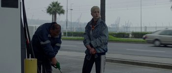 Movie still from “Ema” (2019), directed by Pablo Larraín – A person standing on the side of a road near trees; Medium shot, Over the shoulder angle